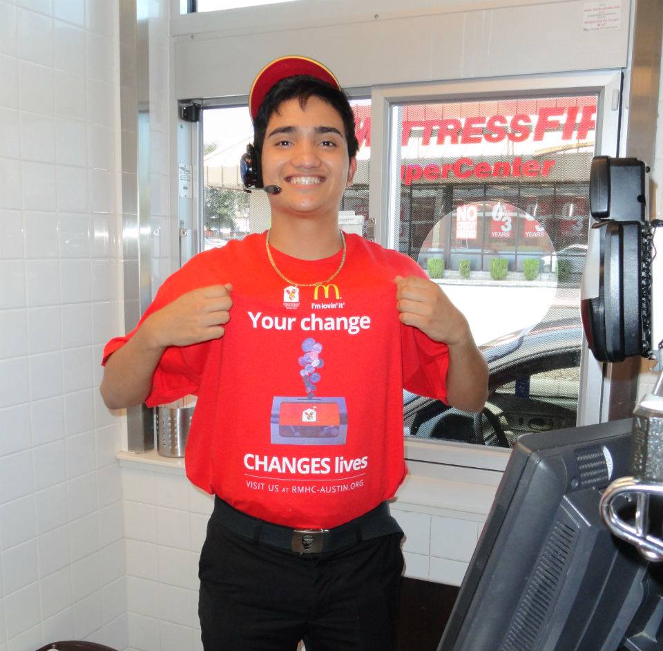 McDonalds employee smiling at the window with a shirt promoting donation box donations