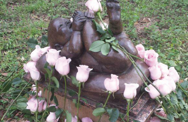 sculpture of young child in memory garden with pink roses placed around it