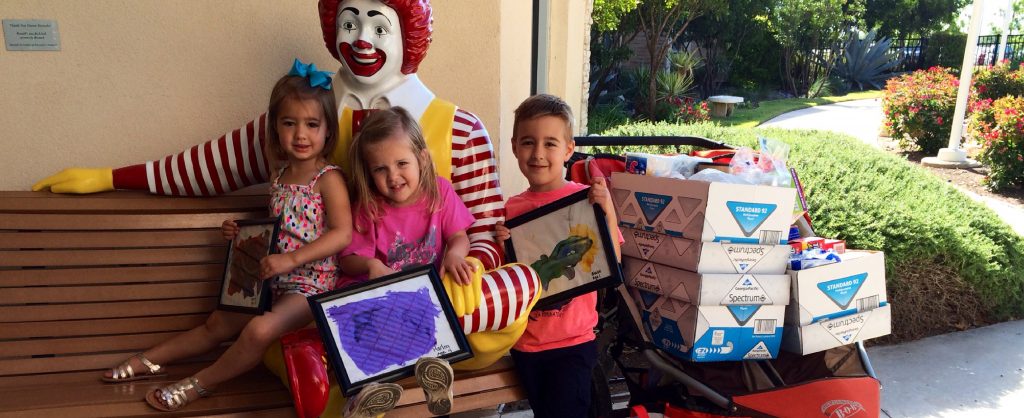 three children sitting with statue of ronald mcdonald with donations for rmhc of central texas